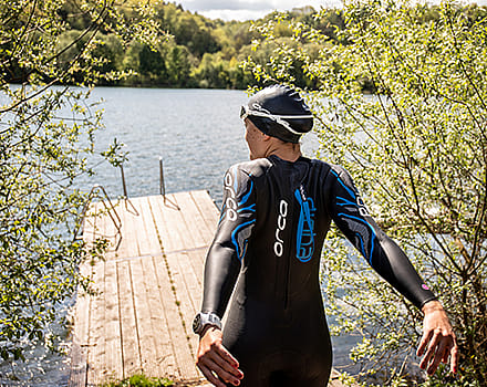 vrouw-op-dock-in-schoolslag-wetsuit-bij-meer
